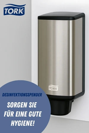 Ein silberner Desinfektionsspender der Marke Tork ist an einer weißen Wand montiert. Im unteren Bereich des Bildes steht in einem blauen Kreis der Text „Desinfektionsspender – Sorgen Sie für eine gute Hygiene!“.