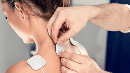 Frau, der die Elektroden eines TENS-Geräts auf den Rücken geklebt werden