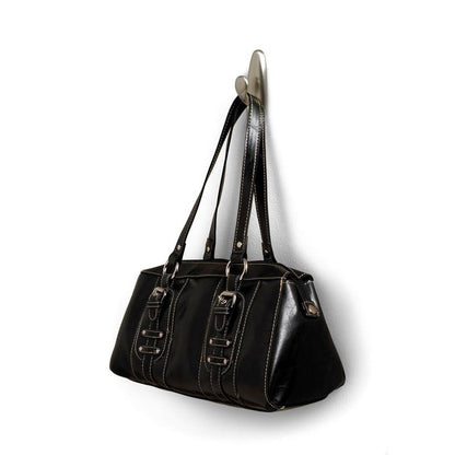 Na metalowym haku Command™ "klasycznym" firmy 3M Deutschland GmbH wisi czarna skórzana torebka z podwójnymi uchwytami i ozdobnymi klamrami. Torebka ma białe szwy i lekko błyszczącą powierzchnię.