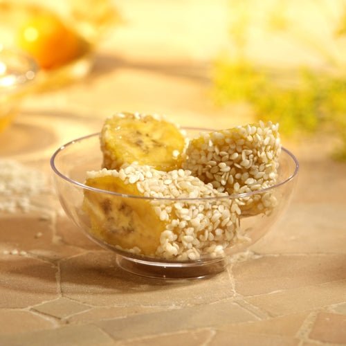 Trzy kawałki banana z białym sezamem są serwowane w miseczce Starpak 50 Fingerfood (PS glasklar), umieszczone na jasnej powierzchni płytek z delikatnie rozmytym tłem – idealne na wydarzenia.