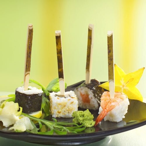 Na PAPSTAR tacce z kartonu (200 sztuk) leżą trzy przekąski sushi na PAPSTAR szaszłykach na przekąski (11 cm drewno naturalne), towarzyszy im karambola, wasabi, imbir i zielenina - idealne na przyjęcia.