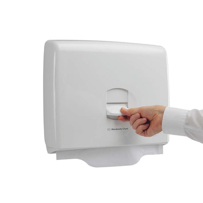 Ręka wyciąga papierowy arkusz z białego dozownika na nakładki na sedes Aquarius™ firmy Kimberly-Clark GmbH, który promuje higienę w publicznych toaletach, na tle prostego białego tła.