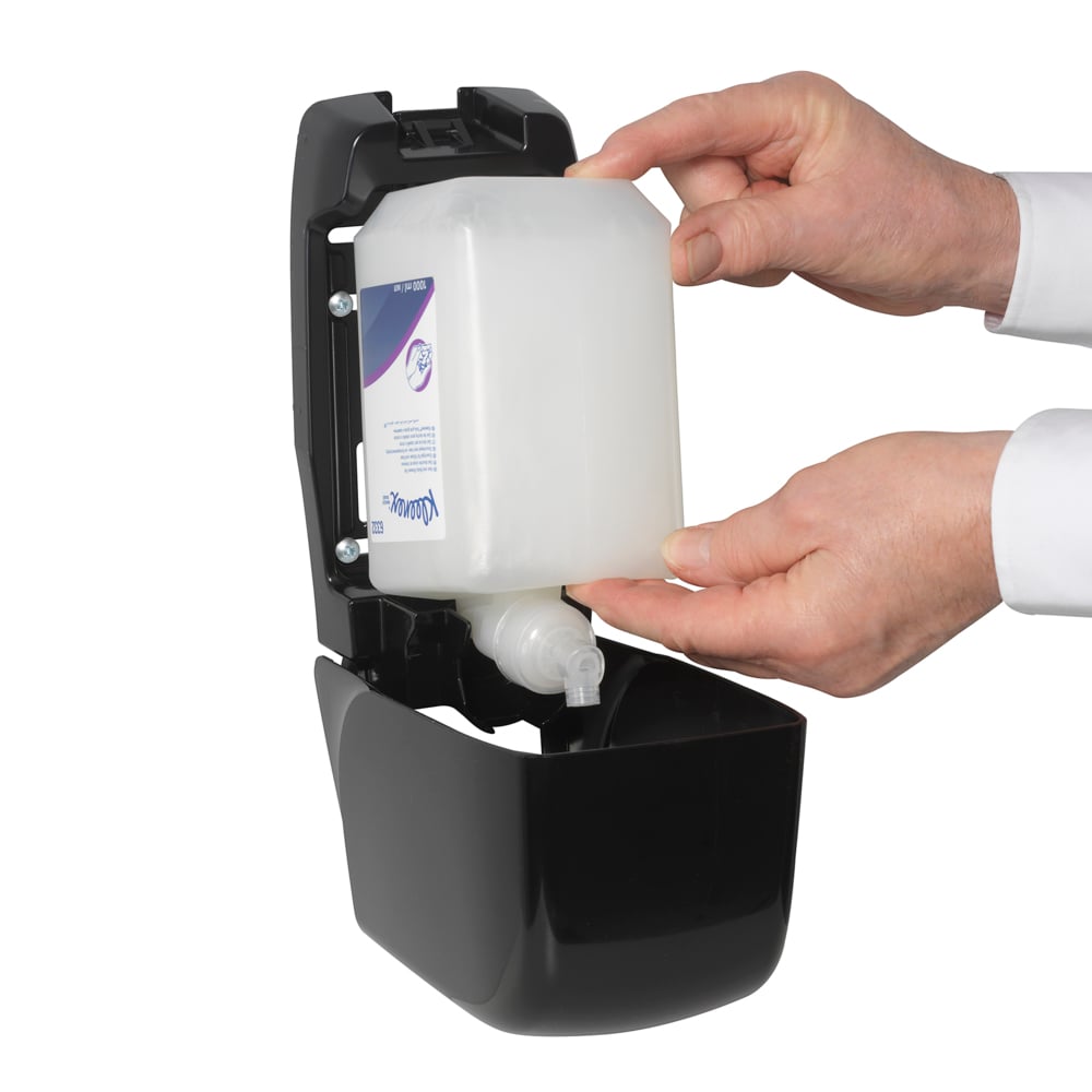Osoba wkłada kasetę z szamponem do włosów i ciała Kleenex® 1L firmy Kimberly-Clark GmbH do otwartego czarnego dozownika ściennego, używając obu rąk, aby zapewnić delikatną pielęgnację i skuteczne czyszczenie.