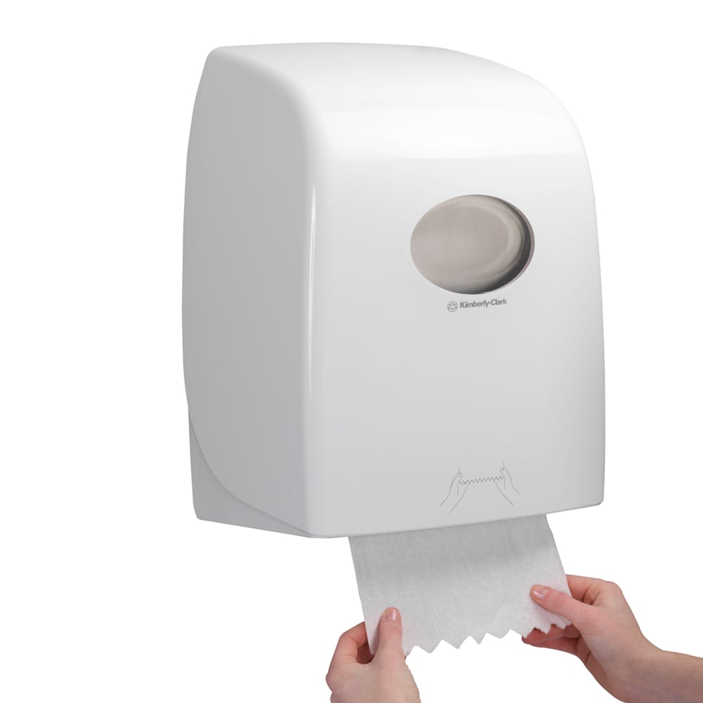 Ktoś wyciąga arkusz Scott® ESSENTIAL™ ręczników - rolka z białego, montowanego na ścianie dozownika Kimberly-Clark GmbH, którego przezroczyste okienko odsłania widok na rolki ręczników wewnątrz.