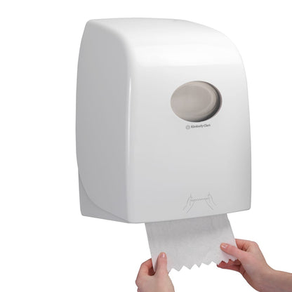 Ktoś wyciąga arkusz Scott® ESSENTIAL™ ręczników - rolka z białego, montowanego na ścianie dozownika Kimberly-Clark GmbH, którego przezroczyste okienko odsłania widok na rolki ręczników wewnątrz.