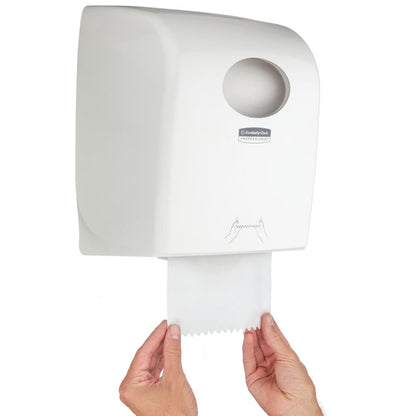 Osoba wyciąga ręcznik papierowy z dozownika ręczników w rolce Aquarius™ - Biały od Kimberly-Clark GmbH z okrągłym otworem i instruktywną grafiką - idealny do miejsc publicznych.