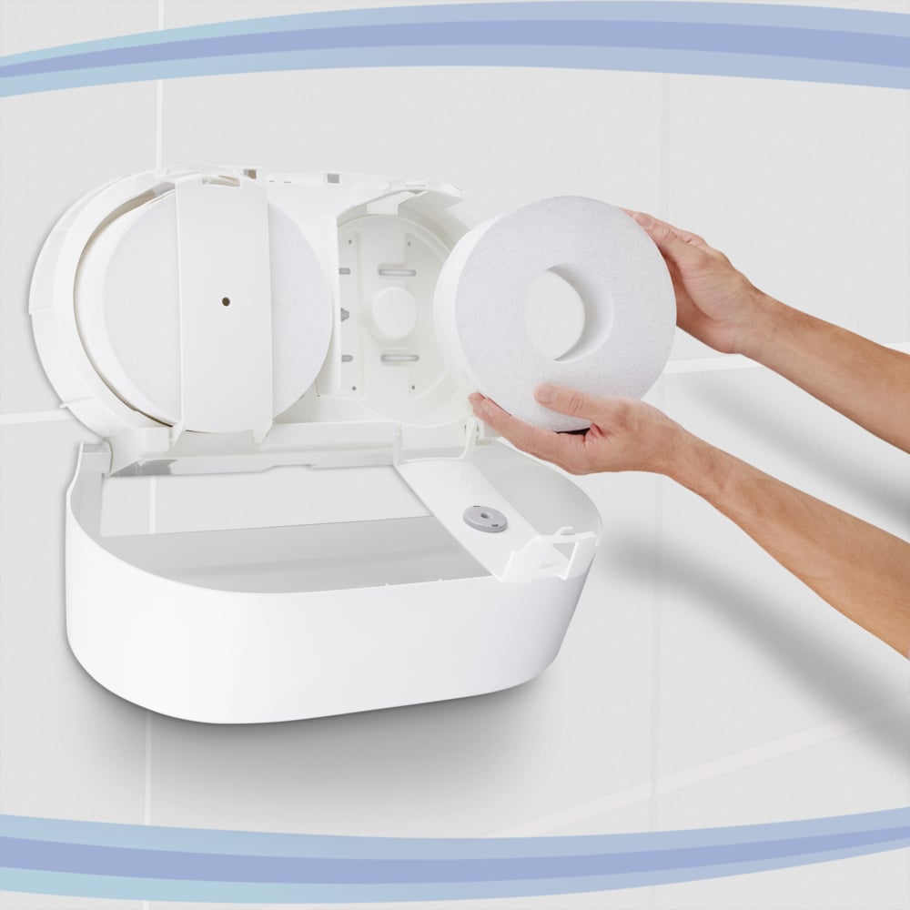 Osoba ładuje dozownik papieru toaletowego Aquarius™ - centralny / biały / Jumbo firmy Kimberly-Clark GmbH, z otwartą pokrywą. Białe wyłożone płytkami ściany i niebieskie krzywe w tle podkreślają praktyczny centralny design dozownika.