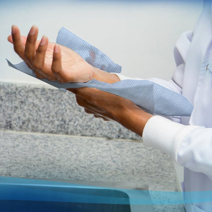 Osoba w białym fartuchu suszy ręce ręcznikami Scott® - rolka (304,00 m x 19,80 cm) od Kimberly-Clark GmbH z rolki papierowych ręczników obok granitowego blatu i zlewu.