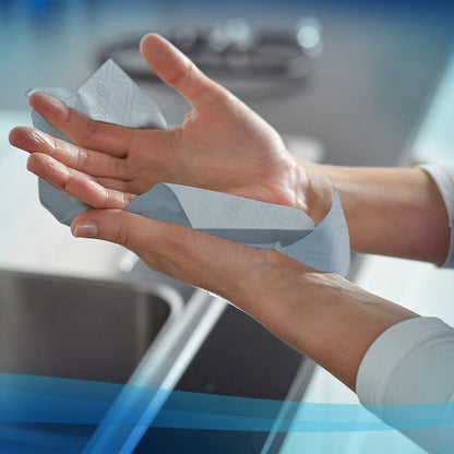 Osoba suszy ręce ręcznikami Scott® Essential™ od Kimberly-Clark GmbH (Rolka/Niebieska - 6 rolek) nad zlewem w nowoczesnej kuchni.