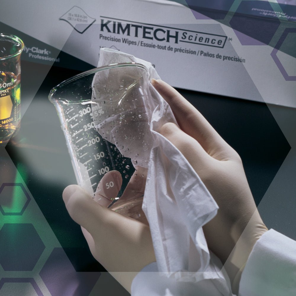 Ręka w rękawiczce wyciera zlewkę białą chusteczką obok pudełka z precyzyjnymi chusteczkami Kimtech® Science firmy Kimberly-Clark GmbH (Duży, Biały, 15x196 chusteczek). W tle widać sprzęt laboratoryjny i inne chusteczki laboratoryjne.