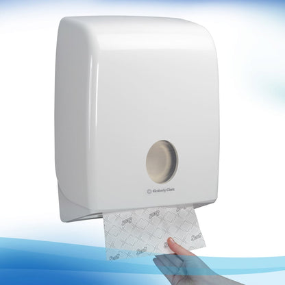 Biały, zamontowany na ścianie dozownik Kimberly-Clark GmbH wydaje pojedynczy arkusz ręczników Scott® - Narrow-Fold / Białe przez metalowe przednie otwarcie, zapewniając higieniczne suszenie rąk przy każdym pociągnięciu.