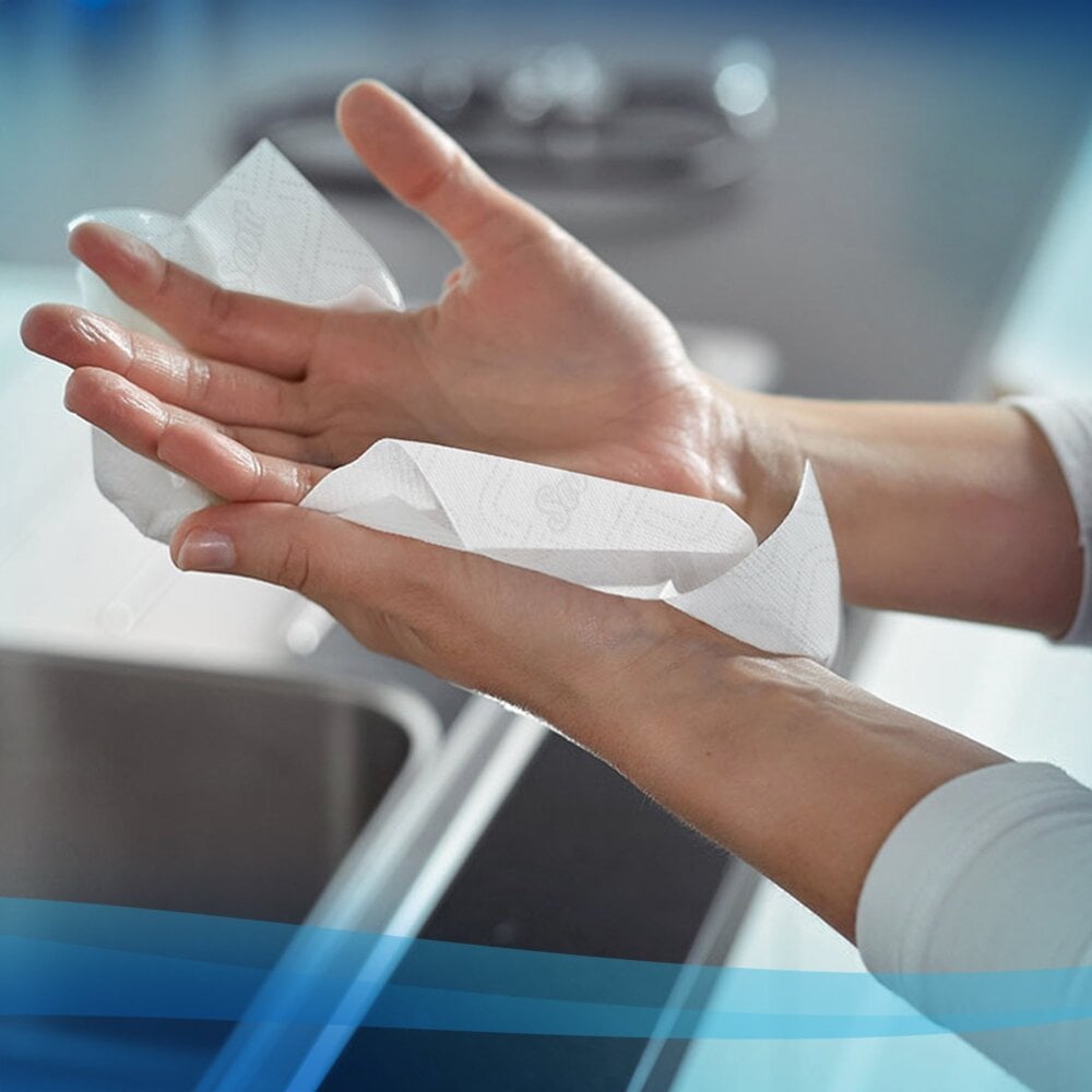 Osoba suszy ręce ręcznikiem w rolce Scott® Essential™ - E-roll Slimroll™ (biały, jednowarstwowy, 6x180m) od Kimberly-Clark GmbH nad zlewem kuchennym - idealny do domu lub łazienek.