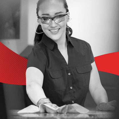 Kobieta w rękawiczkach i okularach uśmiecha się, podczas gdy czyści powierzchnię chusteczką WypAll® X60 General Clean - BRAG™ Box (41,80 × 28,30 cm) firmy Kimberly-Clark GmbH; w tle pojawia się czerwony projekt graficzny.