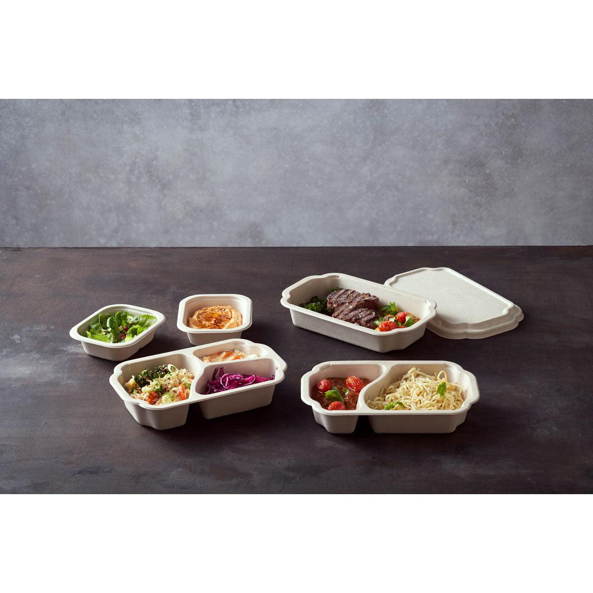 Na ciemnej powierzchni stoją różne pojemniki Tray Side Dish Fibre 1-Comp 55 mm Natur Coated Bagasse firmy Duni GmbH, z których każdy zawiera różne potrawy; opakowanie zawierające 320 sztuk zawiera pojemnik z częściowo otwartą pokrywką.