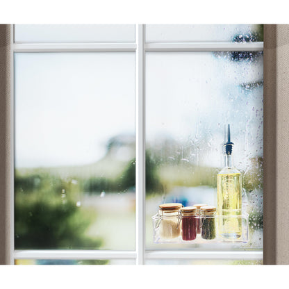 Okno z kroplami deszczu pokazuje scenę na zewnątrz. Na parapecie stoi butelka oleju, trzy małe słoiki ze złotymi pokrywkami i rolka przezroczystej dwustronnej taśmy montażowej Scotch-FIX™ 4910C firmy 3M Deutschland GmbH.