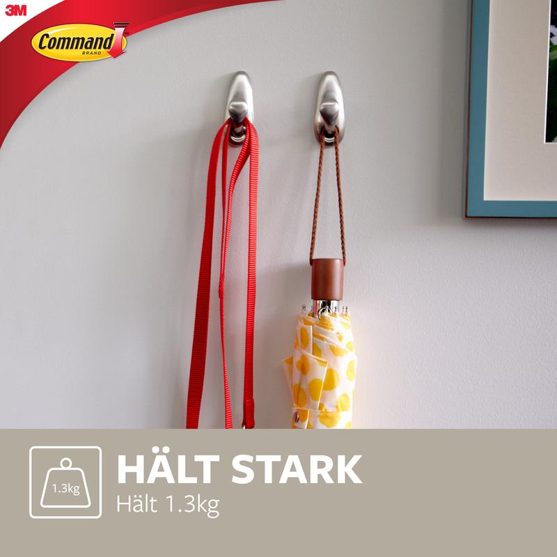 Dwa metalowe haki Command™ "klasyczne" firmy 3M Deutschland GmbH są zamontowane na białej ścianie i trzymają czerwoną smycz oraz żółty wzorzysty parasol. Tekst brzmi: "TRZYMA MOCNO Trzyma 1.3kg" i pokazuje logo Command.