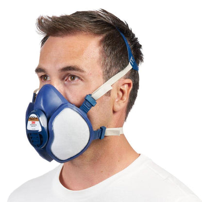 Mężczyzna z profilu nosi maskę ochronną 3M™ z zintegrowanymi filtrami od 3M Deutschland GmbH w kolorach niebieskim i białym z regulowanymi paskami na głowę na prostym białym tle.