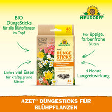 Pudełko Neudorff Shop Azet Düngesticks dla roślin kwitnących jest pokazane wśród kwiatów, z informacjami o 4-miesięcznym działaniu, dostarczaniu żelaza, zawartości organicznej i optymalnym odżywianiu dla żywych kwiatów.