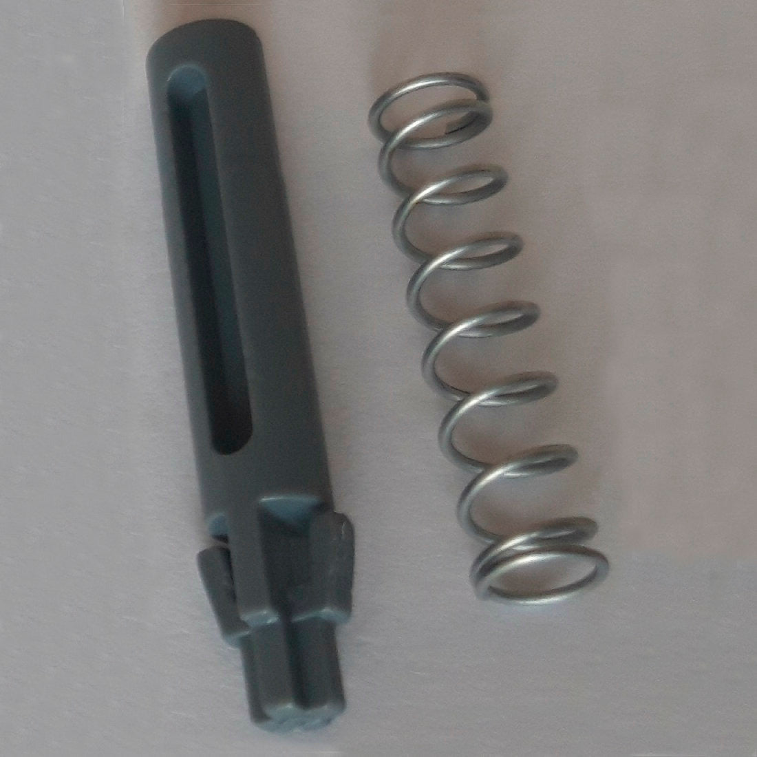 Metalowa sprężyna i ciemnoszary cylindryczny zapasowy trzpień drzwiowy z rowkami i ząbkami, część DI Protect trzpień drzwiowy i sprężyna (1 sztuka) od Diversey Deutschland GmbH & Co. OHG, są przedstawione na jasnej powierzchni i pokazują solidne materiały dla wózka DI Protect.