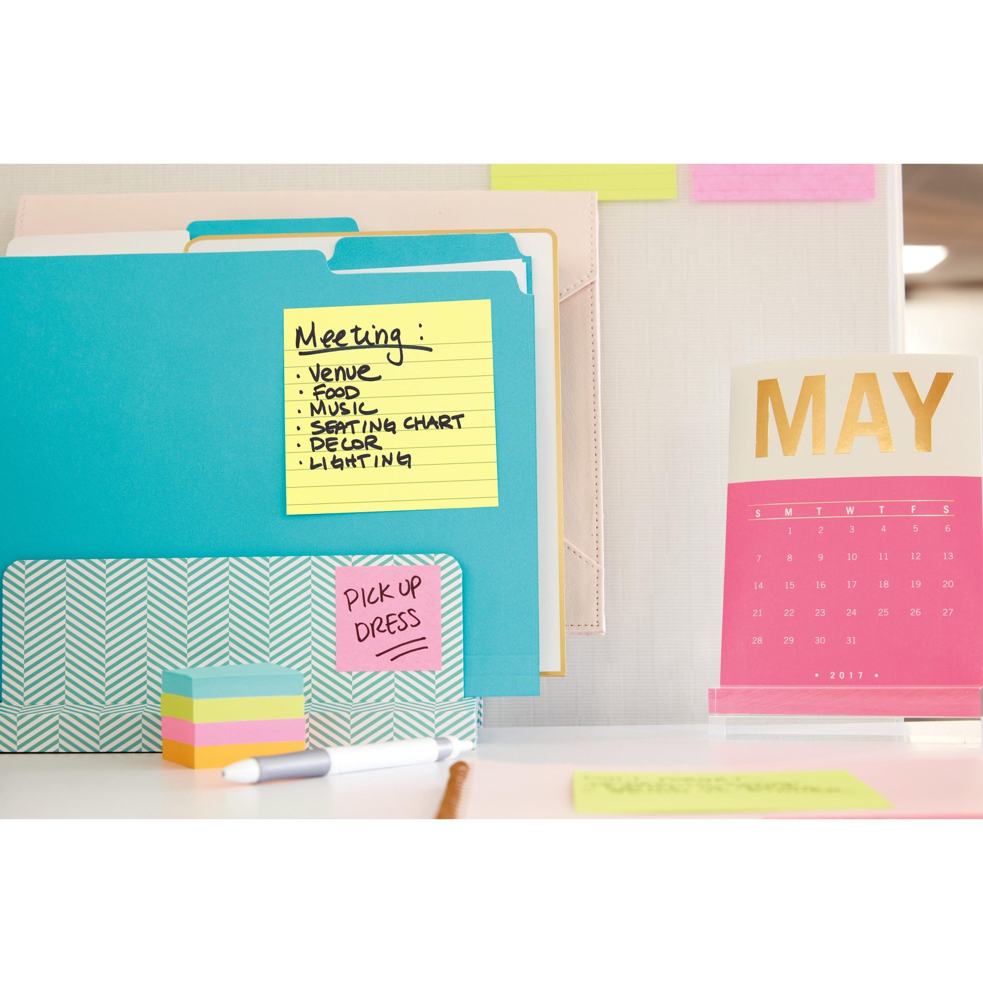 Ein Arbeitsbereich mit 3M Deutschland GmbH Post-it® Notes im Großformat, Gelb (101 mm x 152 mm), Aktenordnern, einem rosa-goldenen Tischkalender für Mai 2017 sowie bunten Haftnotizen und Papieren. Ein Zettel listet "Meeting"-Themen auf, auf einem anderen steht "PICK UP DRESS".