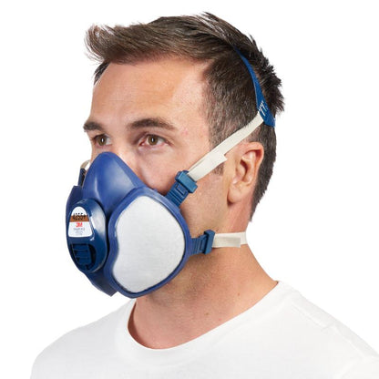 Mężczyzna z krótkimi brązowymi włosami nosi niebiesko-białą maskę ochronną 3M™ z zintegrowanymi filtrami od 3M Deutschland GmbH z regulowanymi paskami, przedstawiony na prostym białym tle.
