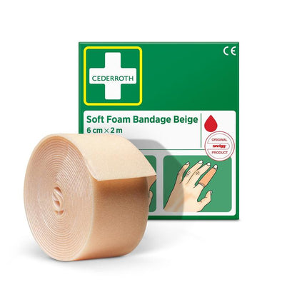 Rolka beżowego bandaża Cederroth-Weichschaumbinde (6 cm x 2 m) od Orkla Wound Care AB jest pokazana przed jego zielono-białym opakowaniem z ilustrowaną instrukcją i czerwonym symbolem kropli.