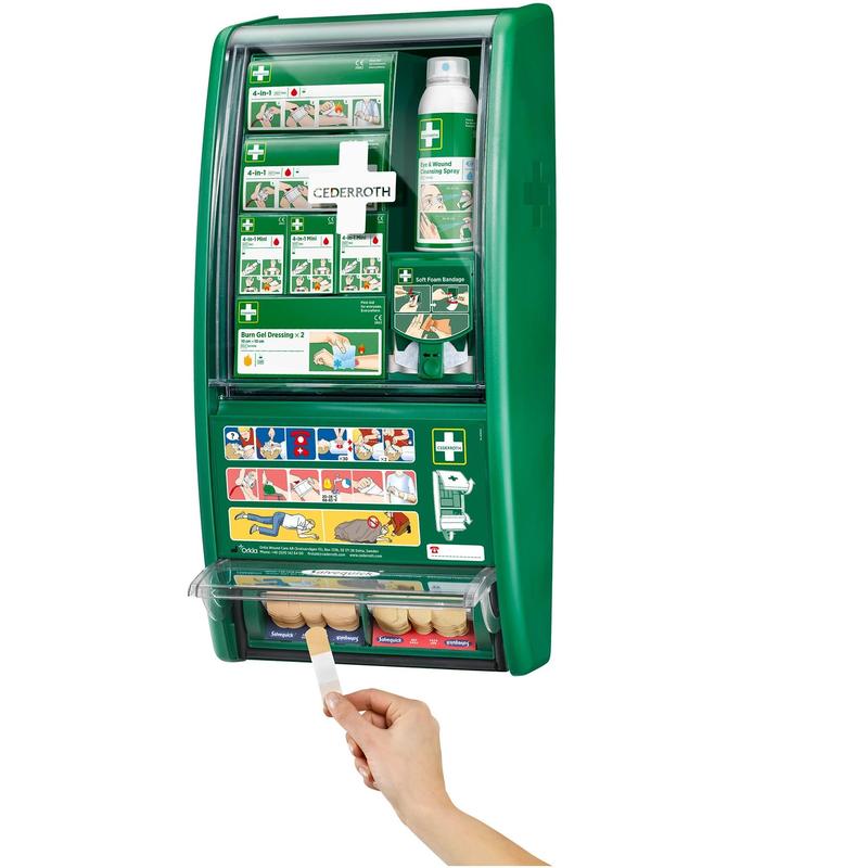 Stacja pierwszej pomocy Cederroth od Orkla Wound Care AB to zielona, montowana na ścianie apteczka z oznakowanymi przegródkami i instruktywnymi obrazkami. Na zdjęciu widać rękę wyciągającą plaster z dolnej przegródki. (1 opakowanie/karton).
