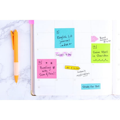 Otwarty planer pokazuje kolorowe karteczki samoprzylepne Post-it® z kolekcji Poptimistic firmy 3M Deutschland GmbH, na których zapisane są terminy i przypomnienia. Po lewej stronie leży pomarańczowy długopis. Każde opakowanie zawiera 12 bloków po 100 kartek, wykonanych w 100% z papieru z certyfikatem PEFC.