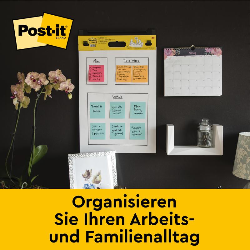 Ściana biurowa z Post-it® Super Sticky samoprzylepnym chart spotkań/flipchart 559 od 3M Deutschland GmbH (63,5 x 76,2 cm), kalendarz miesięczny, półka ze szkłem, orchideą i zdjęciami. Tekst: "Zorganizuj swój dzień.