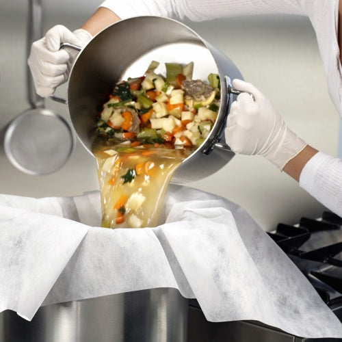 Mit weißen Handschuhen bekleidet gießt jemand Gemüse und Brühe durch mit Pergament ausgelegte Passier- und Filtertücher (100x100 cm, 10 Stück) von Starpak in einen großen Metallbehälter und demonstriert so die praktische Anwendung in der Küche.