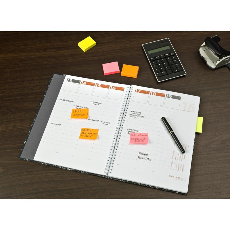 Otwarty planer z odręcznymi notatkami i kolorowymi karteczkami Post-it® w różnych kolorach neonowych (38 mm x 51 mm, 100 arkuszy/blok, 3 bloki/opakowanie, 100% PEFC) od 3M Deutschland GmbH na drewnianym stole z długopisem, kalkulatorem i dyspenserem taśmy klejącej.