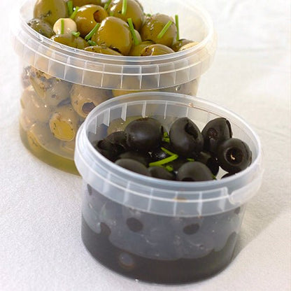 W dwóch przezroczystych pojemnikach Starpak 30 na delikatesy (770 ml, PP, Ø 11,8 cm · 11,3 cm) z oryginalnym zamknięciem umieszczono oliwki na białym tle – w tylnym pojemniku zielone oliwki z ziołami, a z przodu czarne oliwki z dekoracją ziołową.