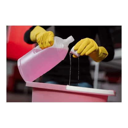 Osoba nosząca rękawice ochronne AMPri SolidSafety ChemL firmy AMPri Handelsgesellschaft mbH wlewa płyn z przezroczystej plastikowej butelki do małej pokrywki nad różowym pojemnikiem. Płyn, prawdopodobnie roztwór czyszczący AMPri, wyróżnia się na rozmytym tle.