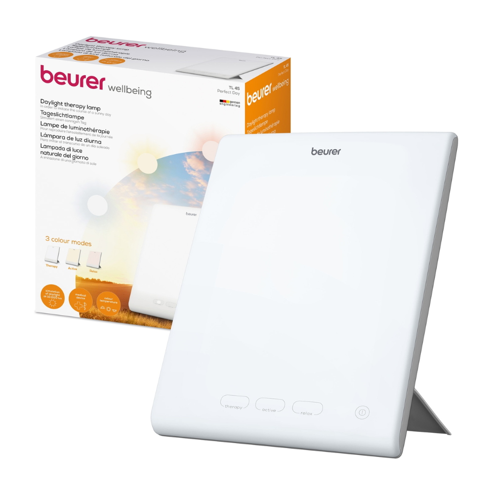 Biała Beurer Perfect Day lampa dzienna TL 45 od Beurer GmbH jest pokazana obok swojego opakowania. Na opakowaniu znajduje się nazwa produktu i opis w kilku językach, prezentowane są różne tryby temperatury barwowej. Lampa ma prosty design z przyciskami z przodu, co czyni ją idealną do regulacji Twojego rytmu dobowego.