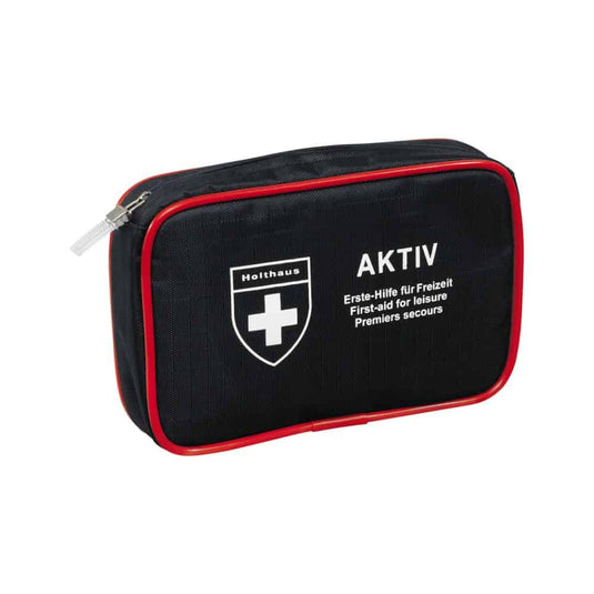 Kompaktowa, czarna apteczka pierwszej pomocy z czerwonymi wykończeniami i zamkiem błyskawicznym, z białym logo w kształcie krzyża oraz napisami „Holthaus Medical AKTIV” i „Erste-Hilfe für Freizeit / First-aid for Leisure / Premiers secours” z przodu. Idealna zarówno w podróży, jak i w domu.