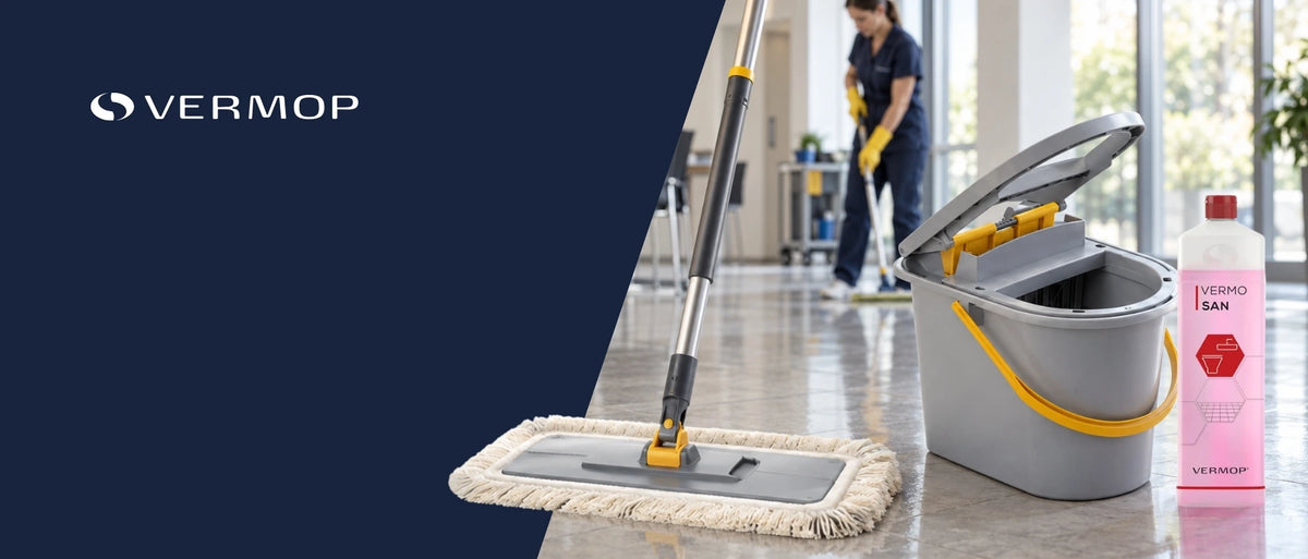 VERMOP Reinigungssystem mit Flachmopp, grauem Eimer und Reinigungsmittel vor einem professionellen Reinigungseinsatz. Im Hintergrund wischt eine Reinigungskraft einen Boden.