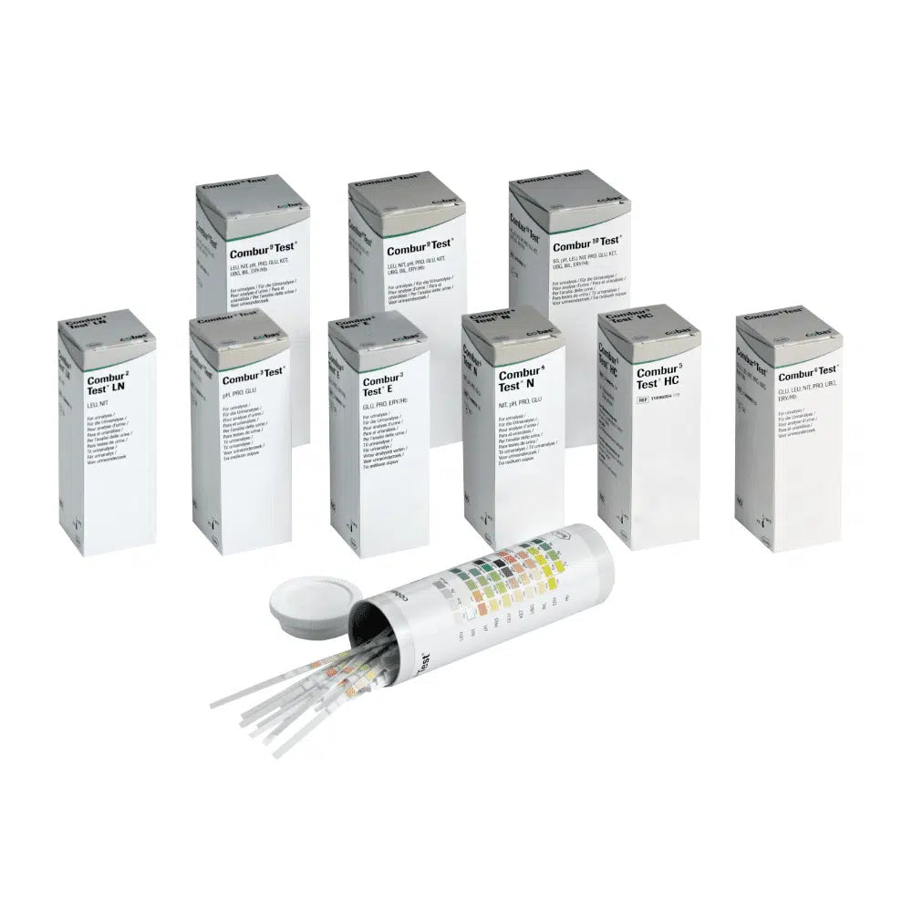 Za otwartym cylindrycznym pojemnikiem z pokrywką kryje się dziewięć pudełek z napisem „Combur®“ firmy Servoprax GmbH, z których każde zawiera 100 pasków testowych do moczu Roche. Z boku pojemnika znajduje się wielokolorowa tabela, idealna do przeprowadzania szybkiego testu.