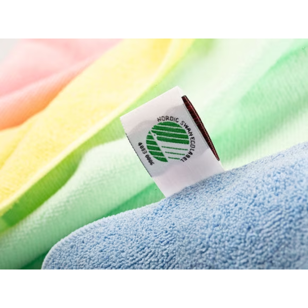 Nahaufnahme eines Stoffetiketts auf einem Vileda Professional MicroTuff Plus-Handtuch mit dem Symbol des Nordic Swan Ecolabel. Das Handtuch weist sanfte Farbtöne in Gelb, Rosa, Grün und Blau mit sichtbarer Textur auf und ist daher ideal für die professionelle Reinigung. Es wird von der Vileda GmbH hergestellt und ist als nachhaltiges Mikrofasertuch bekannt.