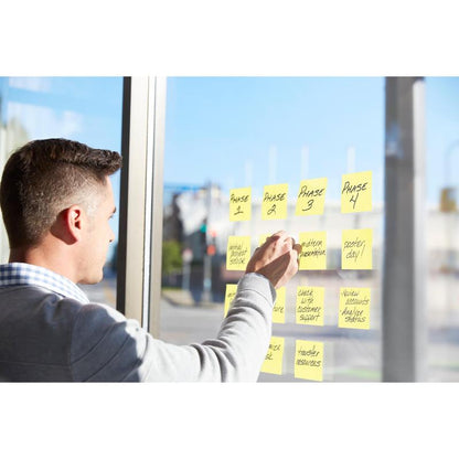 Osoba używa karteczek Post-it® Super Sticky Notes (76 x 76 mm, 90 arkuszy, certyfikat PEFC) firmy 3M Deutschland GmbH do organizowania faz projektu na szklanym oknie, przez które wpada światło słoneczne i z którego widać ulicę.