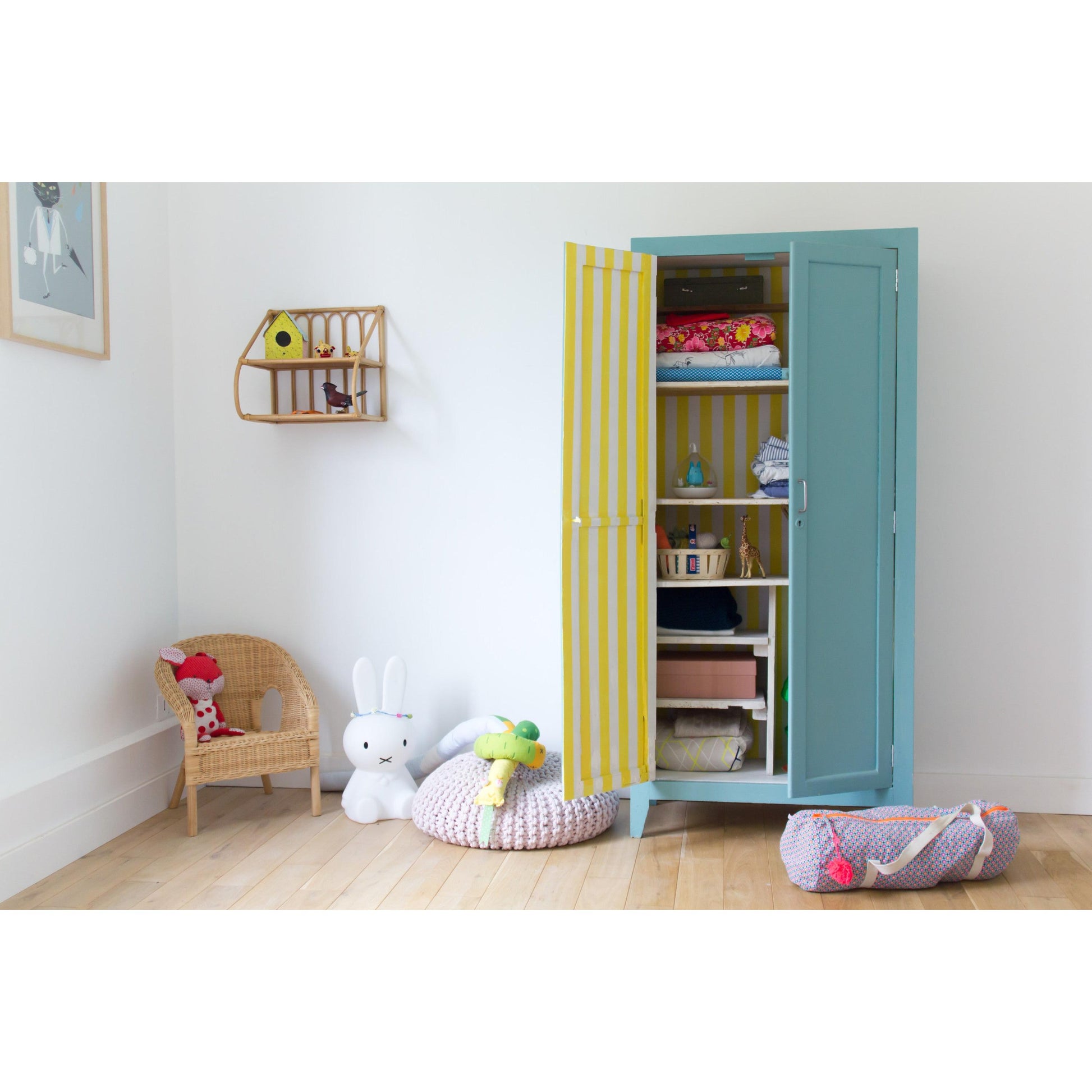 Ein aufgeräumtes Kinderzimmer mit blauem Kleiderschrank, einem Korbstuhl mit Spielzeug, Kuscheltieren auf dem Boden und Dekoration - ideal, um empfindliche Oberflächen mit Scotch® Malerabdeckband von 3M Deutschland GmbH (24 mm x 41 m, 1 Rolle) zu schützen.
