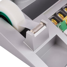 Zbliżenie na organizer biurkowy Post-it® firmy 3M Deutschland GmbH z karteczkami Post-it®, indeksami i taśmą klejącą Scotch® Magic™ (1 sztuka), pokazujący podajnik taśmy z ząbkowaną krawędzią oraz sąsiednie przegródki organizera biurkowego.