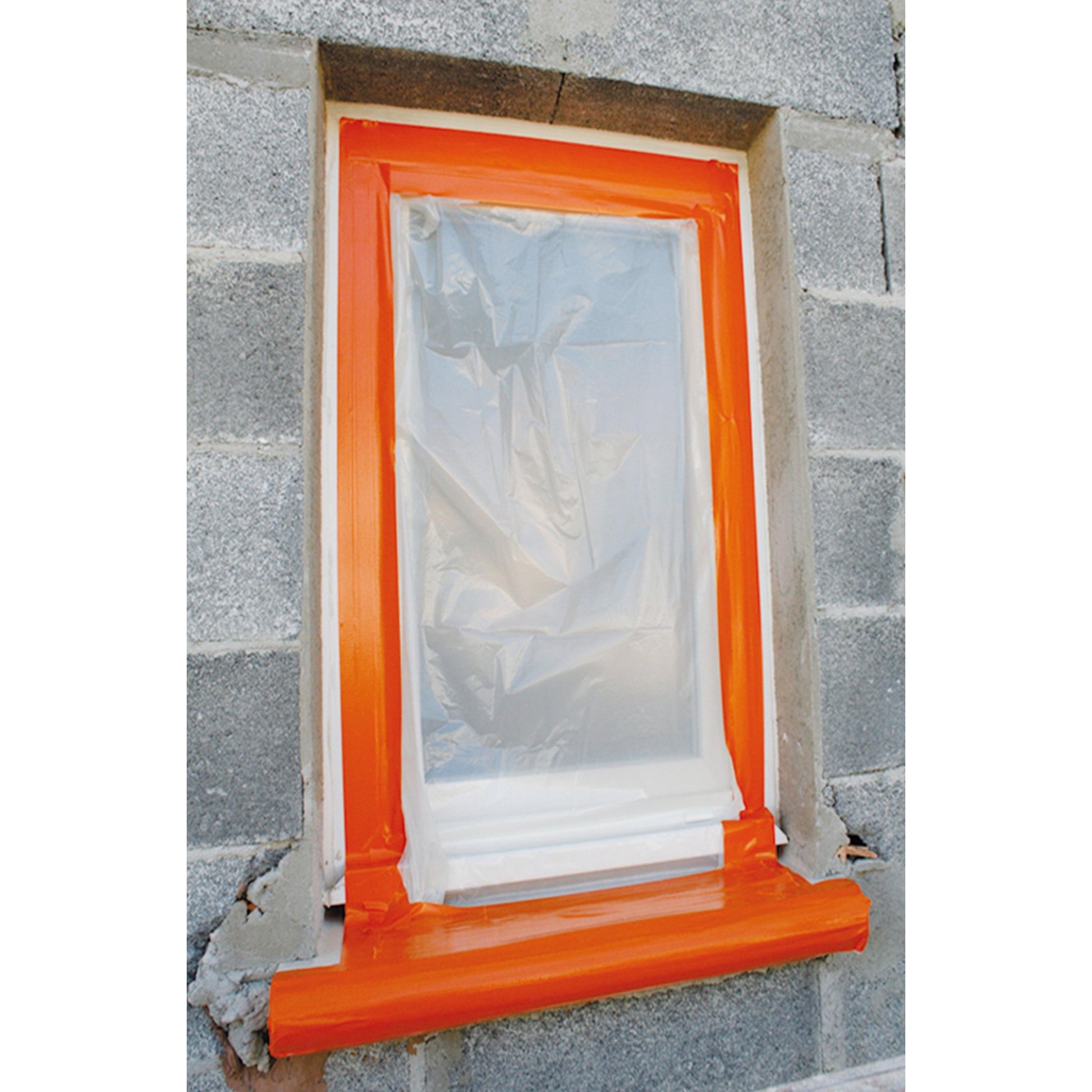 Eine Fensteröffnung in einer Schlackenwand ist mit Kunststoff abgedeckt, gesichert mit 3M Deutschland GmbH Scotch® High Visibility Klebeband, orange (25 m x 48 mm). Die unfertige Wand und der Rahmen weisen an der Basis einige Schäden auf.