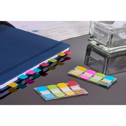 Post-it® Index Strong Ablagetabs od 3M Deutschland GmbH w kolorach niebieskim, fioletowym, różowym i żółtym (15,8 mm x 38,1 mm) są przymocowane do niebieskiego segregatora; na stole leżą dwa opakowania do efektywnej organizacji dokumentów.