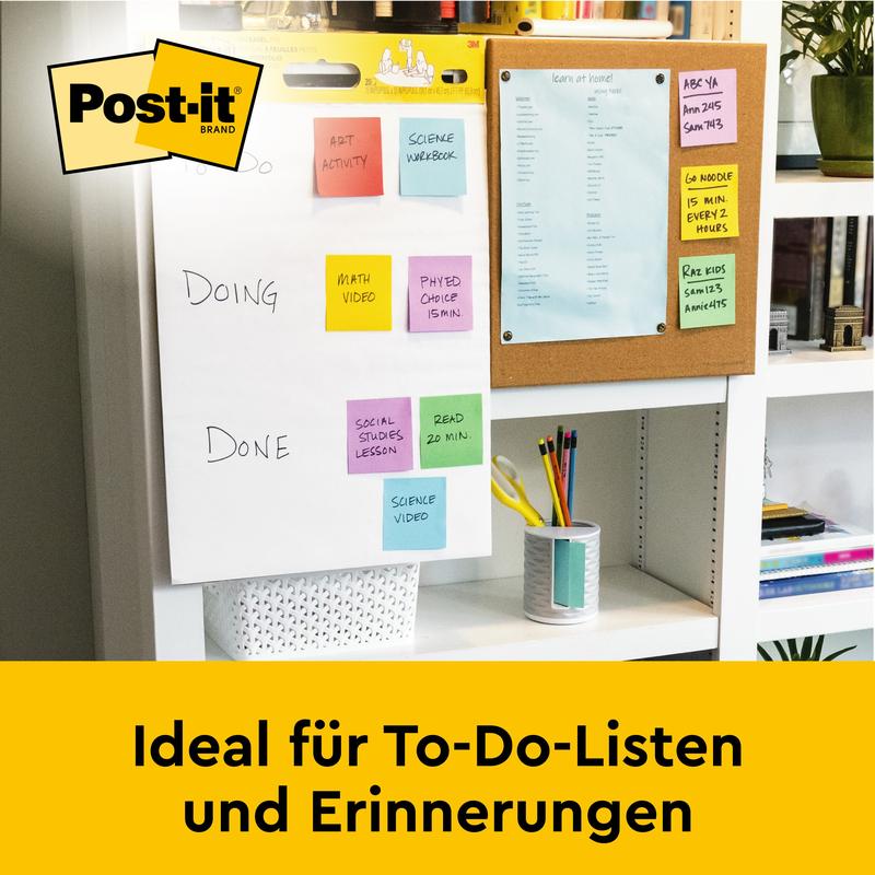 Na biurku stoi Post-it® Super Sticky samoprzylepny chart spotkań/flipchart od 3M Deutschland GmbH (biały, 63,5x76,2 cm), idealny do list zadań i przypomnień. W tle: tablica korkowa z niebieskim papierem.