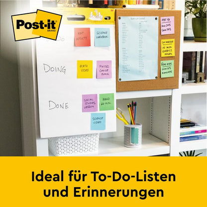 Na biurku stoi Post-it® Super Sticky samoprzylepny chart spotkań/flipchart od 3M Deutschland GmbH (biały, 63,5x76,2 cm), idealny do list zadań i przypomnień. W tle: tablica korkowa z niebieskim papierem.