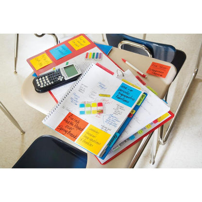Na biurku w klasie leżą zeszyty, planer z 3M Post-it® Index Strong Ablagetabs (Mini, żółty, czerwony, niebieski i zielony), kalkulator, długopisy, zakreślacze i teczki; otaczają je puste krzesła, a zakładki pomagają organizować dokumenty.