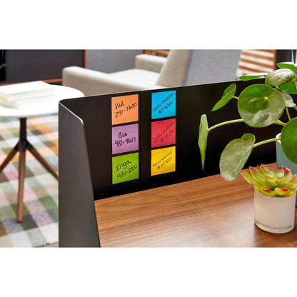 Czarny metalowy dzielnik na drewnianym stole prezentuje sześć opakowań karteczek Post-it® od 3M Deutschland GmbH, żółte, 76x76mm, 90 arkuszy/blok, certyfikowane przez PEFC. Zielone rośliny doniczkowe zdobią biurko, w tle znajdują się książki i krzesło.
