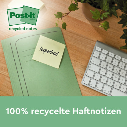 Zielony segregator z żółtymi Post-it® Recycling Notes, żółte, 76x127mm, 100 kartek/blok od 3M Deutschland GmbH leży na drewnianym biurku obok białej klawiatury i rośliny. Kartki są w 100% PEFC (SGSCH-PEFC-COC-110078) i przyjazne dla środowiska.