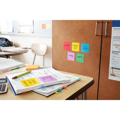 Biurko w klasie z notatnikami, kalkulatorem i kolorowymi karteczkami samoprzylepnymi. Na szafce znajdują się karteczki samoprzylepne 3M Post-it® (żółte, 76x76mm, 90 arkuszy/blok, 6 bloków/opakowanie, 100% PEFC) z nazwami przedmiotów: geometria, językoznawstwo, nauki społeczne, biologia i hiszpański.