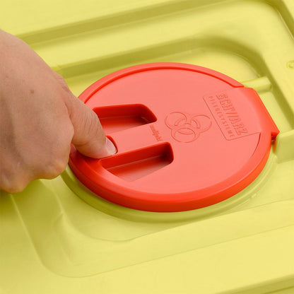 Ręka naciska na czerwoną pokrywkę żółtego 12-litrowego pojemnika na odpady Helmut Schwarz GmbH melijekt (20 sztuk na karton), na którym jest wytłoczone symbol biohazardu oraz napis "SHARPMAX".